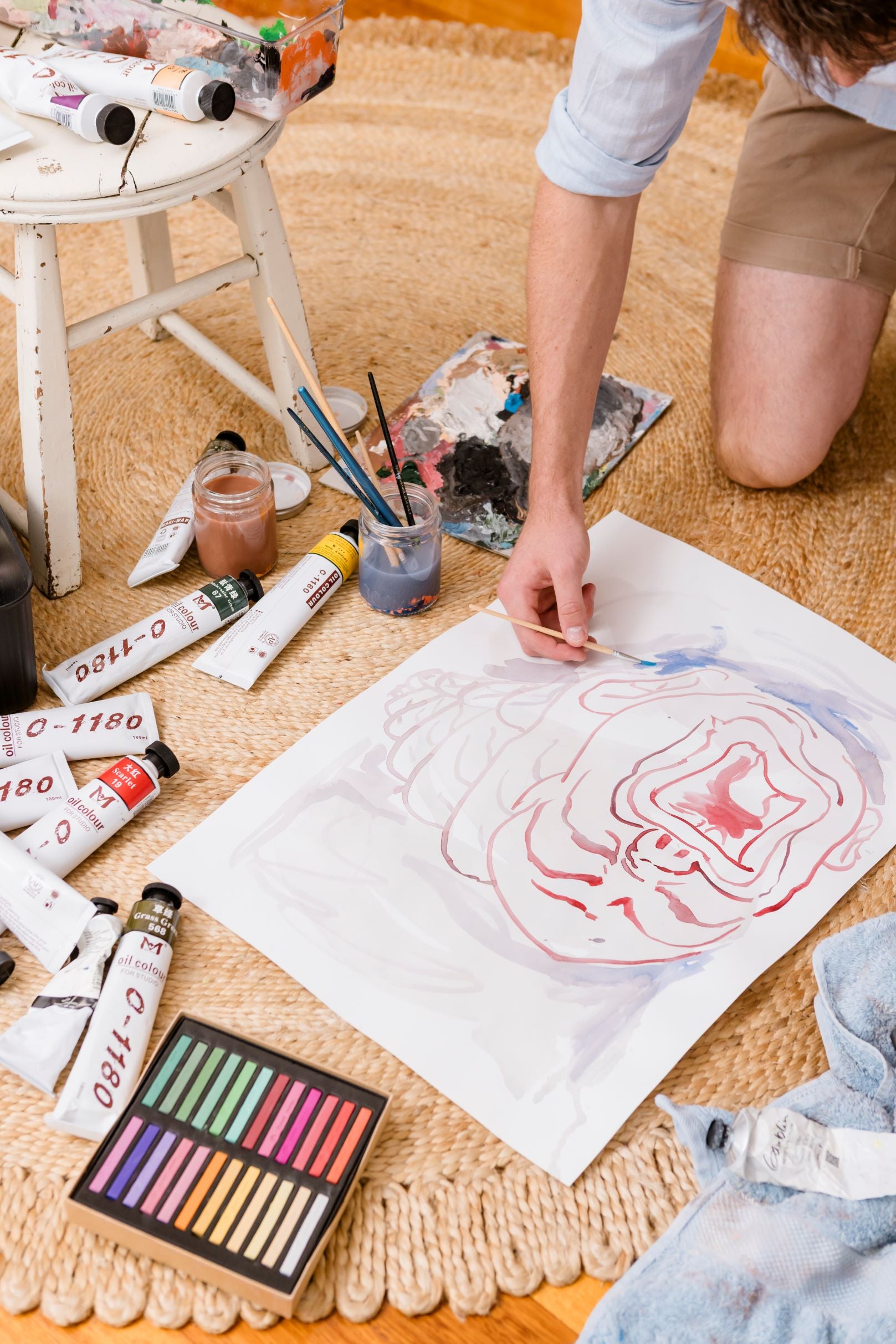 Person drawing on a piece of paper with art supplies around