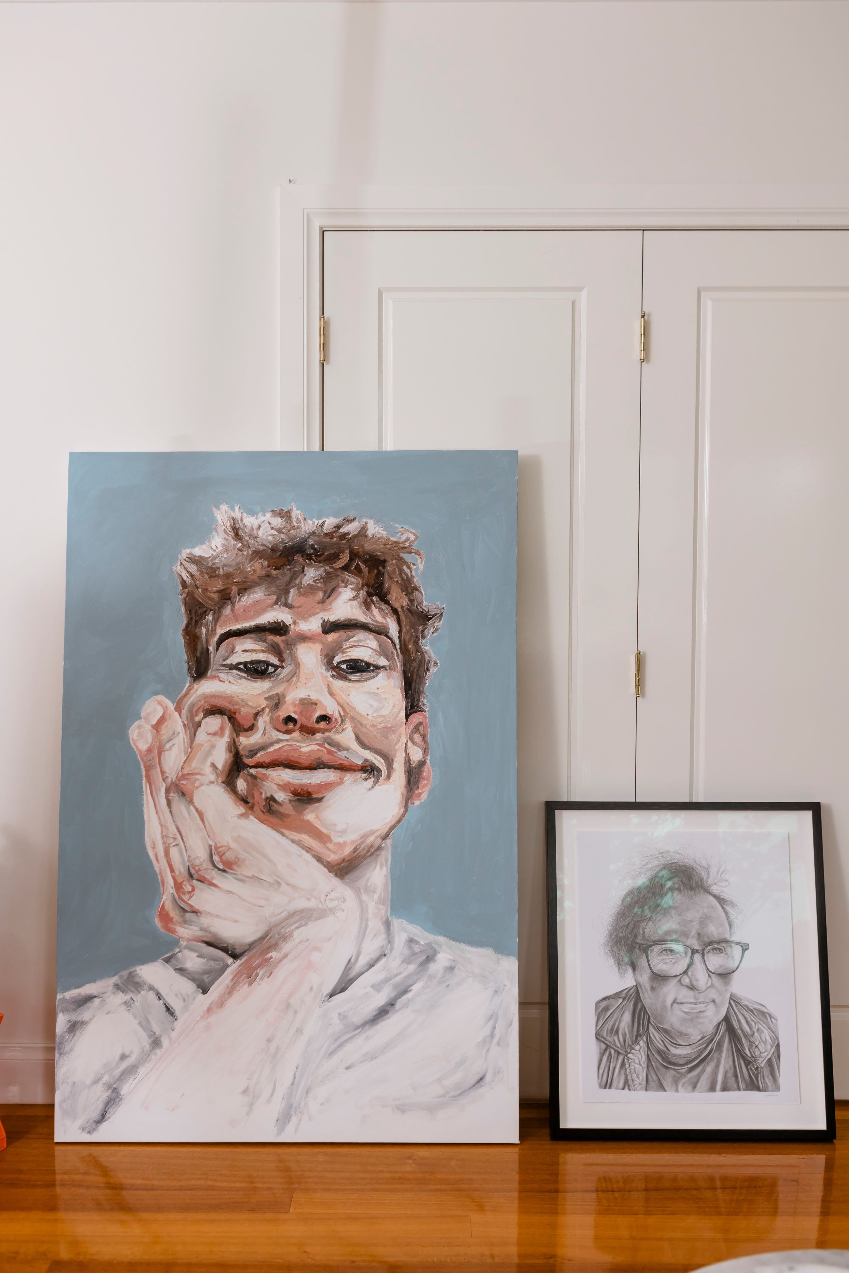 Two framed portraits on a wooden surface with a white wall in the background