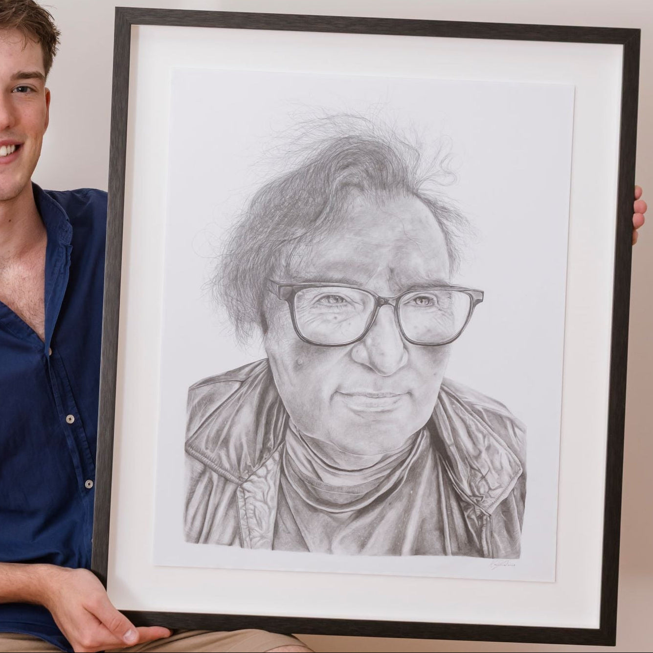 Person holding a framed portrait of another person against a white wall